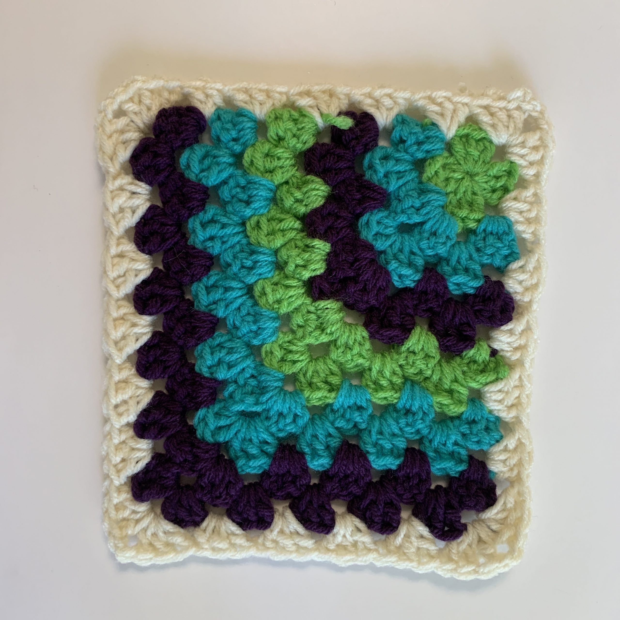 mitered granny square crocheted iwth green blue purple and white yarns